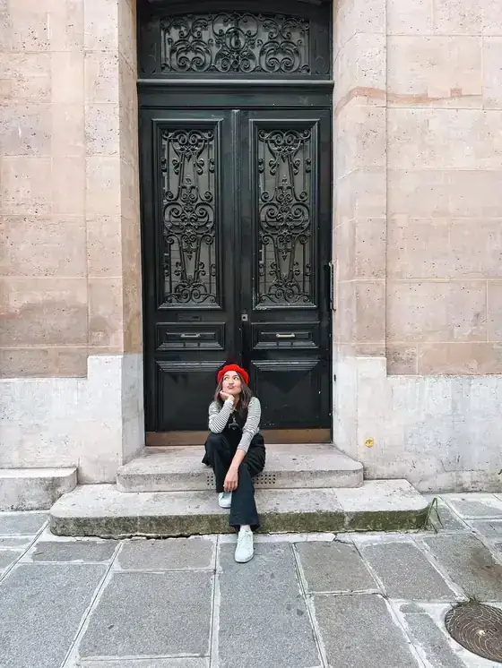 Página do guia: Camila sentada diante de uma porta preta parisiense