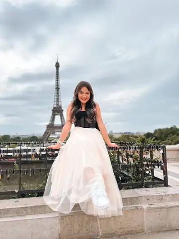 Camila de saia de tule sentada num muro, diante da Torre Eiffel