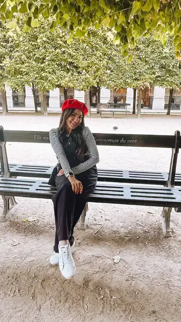 Camila de boina vermelha sentada num banco de jardim