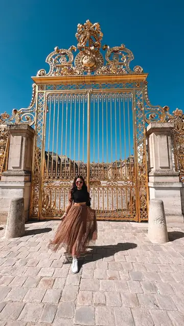 Camila diante do portão dourado de Versalhes